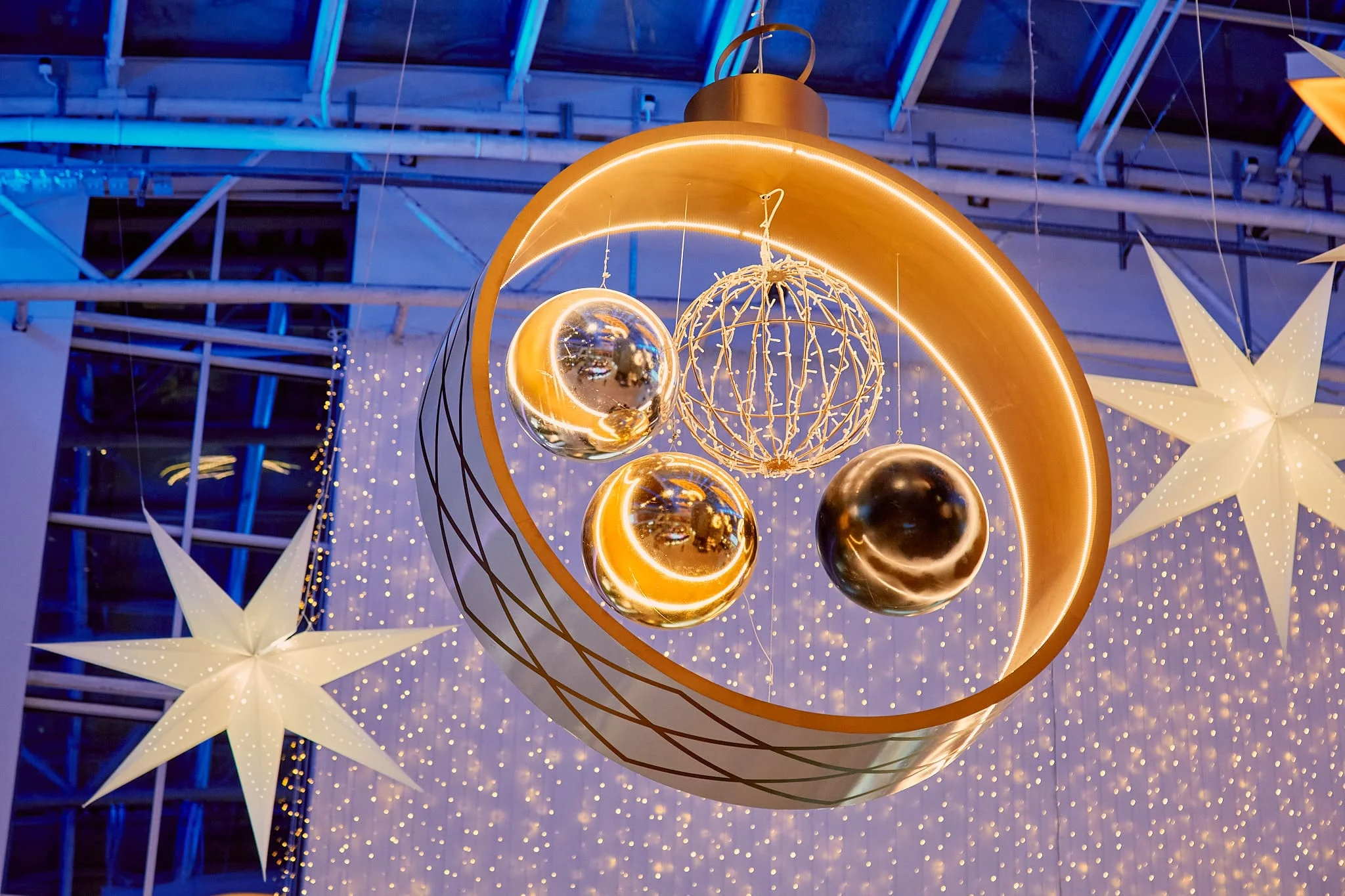 Una media luna dorada con esferas de acabado espejo y una esfera luminosa en su interior, como pieza dominante del atrio de un centro comercial