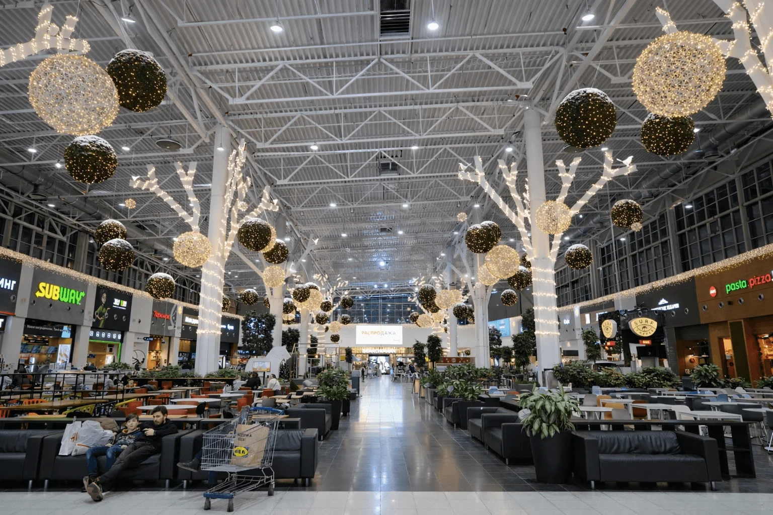 La zona de restauración de un centro comercial bajo árboles de luz y esferas suspendidas: una familia descansa en un sofá entre luz cálida